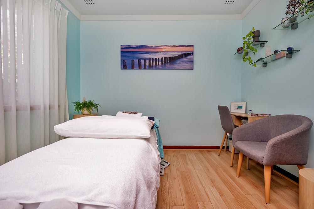 A Bowen Therapy room with massage table, desk and chair nicely decorated with natural plants and wall painting