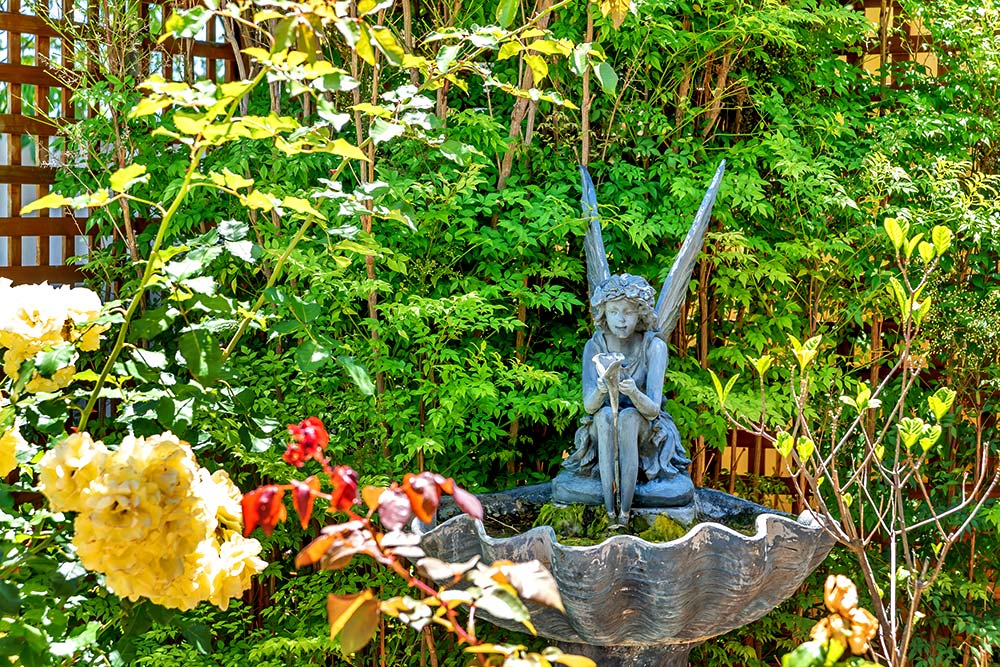 Fairy garden statue amongst yellow flowers and greenery